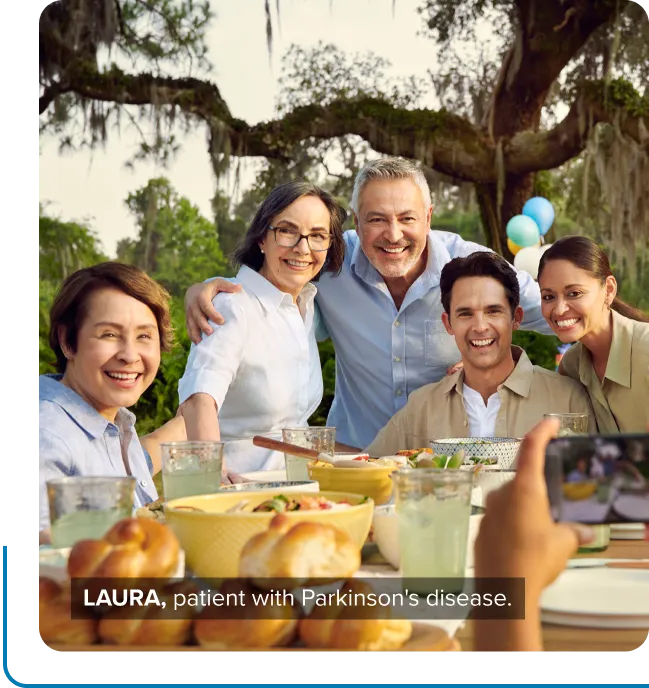 Laura, a patient with Parkinson’s disease, smiling at the table with her friends and family